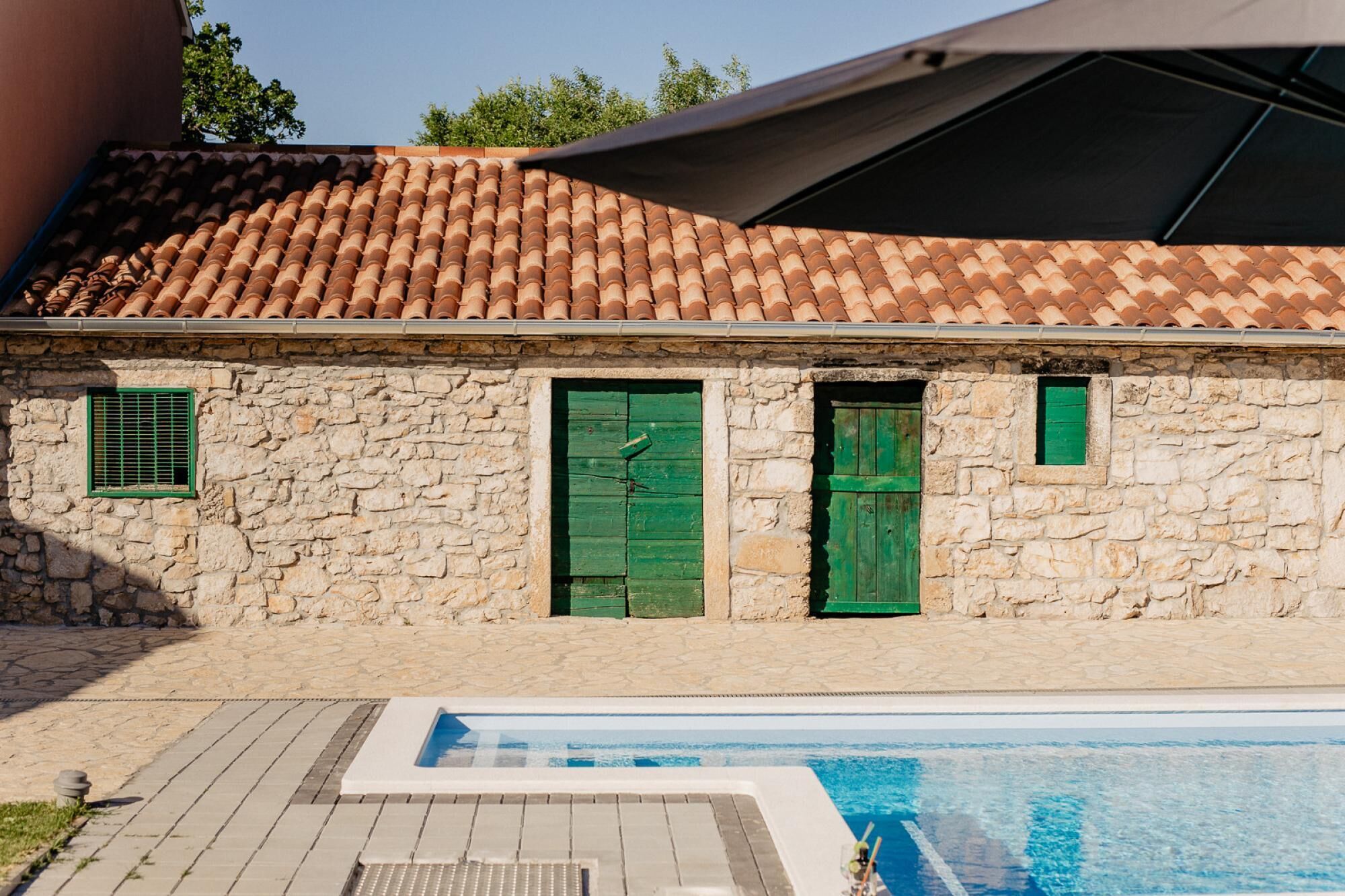 A stone building with a tiled roof, a pool, and a covered area.