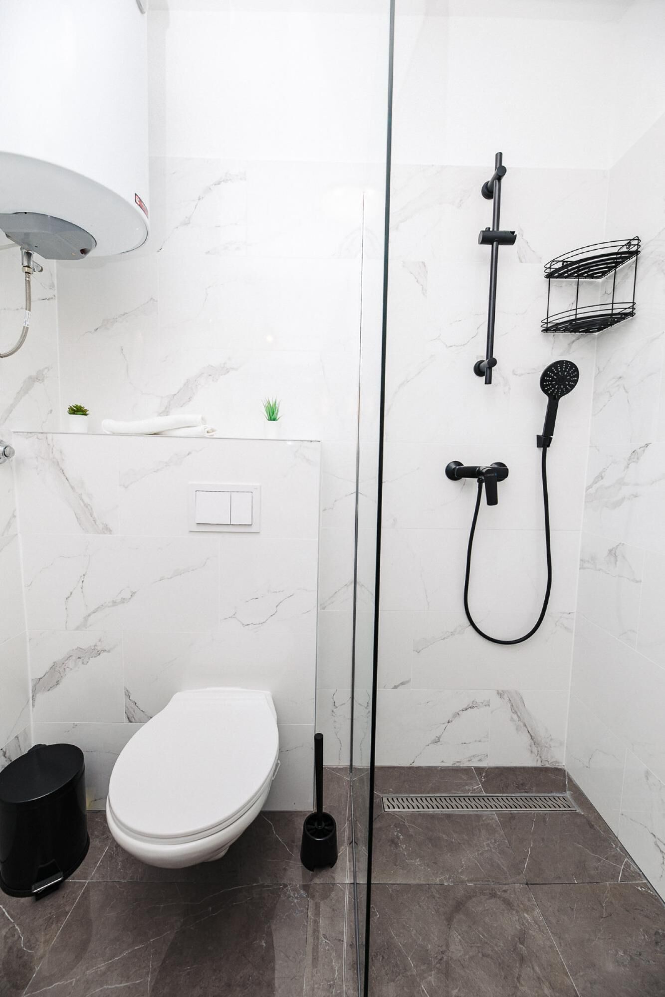 A modern bathroom with a glass-enclosed shower, a toilet, and a small trash bin.