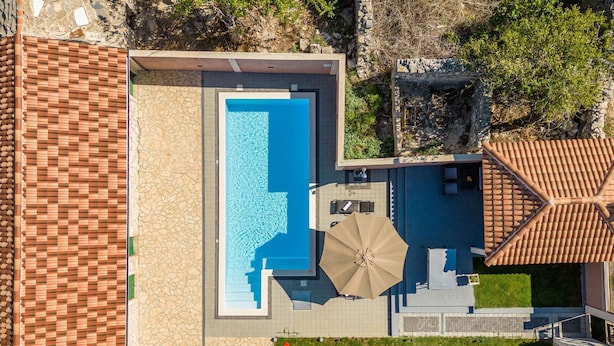 An aerial view of a modern house with a rectangular swimming pool, a patio area with a table and umbrella, and a stone wall. - Villa Moki Zadarvillas (Benkovac)