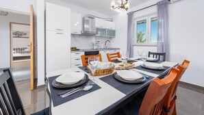 A modern kitchen with white cabinets, a built-in oven, and a dining area with a table set for four. - Villa Moki Zadarvillas (Benkovac)