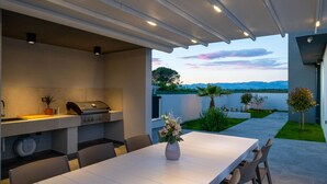 An outdoor dining area with a grill, chairs, and a table. - Villa Oasis Zadarvillas (Zadar)
