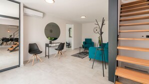 A modern living room with a staircase, a round mirror, a teal sofa, and a coffee table.