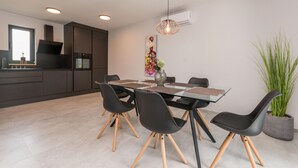 A modern kitchen with dark cabinetry, a central island, and a dining area with a glass table and black chairs.
