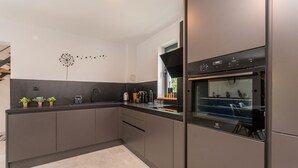 A modern kitchen with dark cabinetry, a built-in oven, and a window providing natural light.