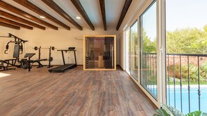 Une salle de sport spacieuse dotée d’un plancher en bois, d’équipements d’exercice et d’une grande fenêtre donnant sur une piscine.