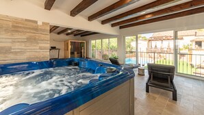 Un bain à remous dans un espace intérieur spacieux, agrémenté de poutres en bois, de grandes fenêtres et offrant une vue sur une piscine et un espace extérieur.