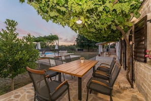 An outdoor patio with a wooden table and chairs, surrounded by stone walls and greenery. - Villa Vitis Zadarvillas (Promina)