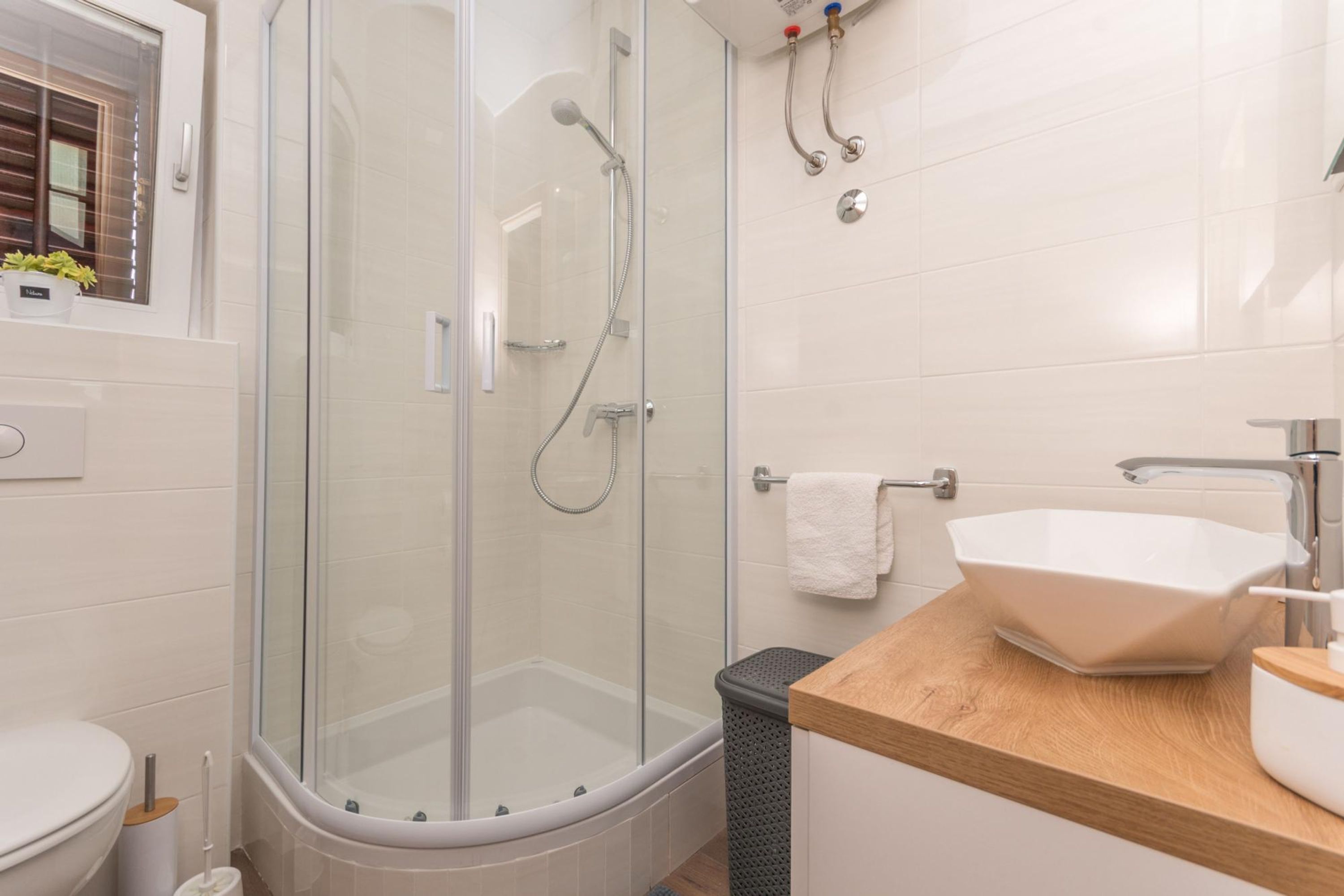 Une salle de bain moderne avec une douche à parois de verre, un lavabo blanc et un plan de toilette en bois.