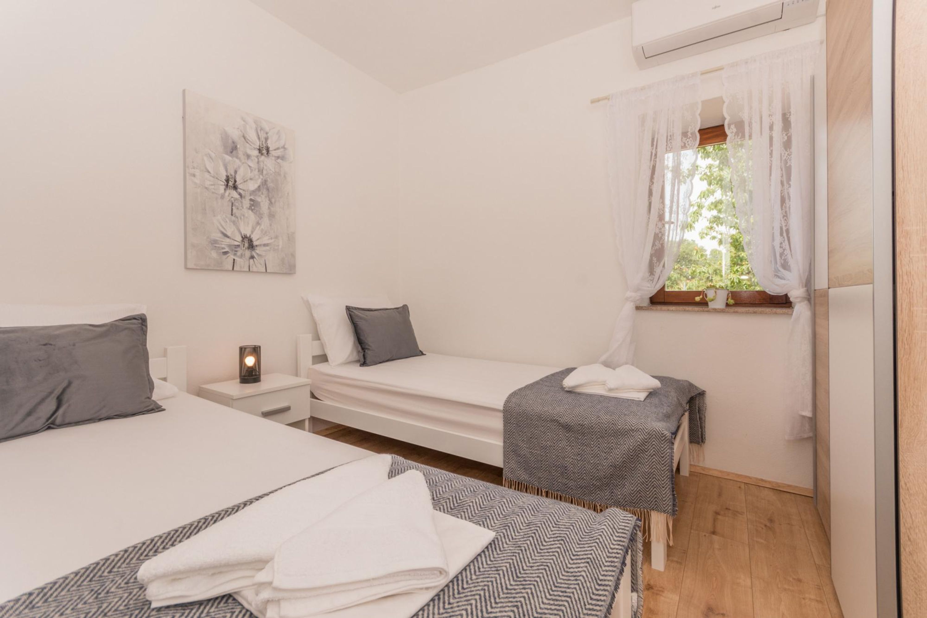 A bedroom with a bed, a bedside table with a lamp, a small table with a chair, and a window with curtains.