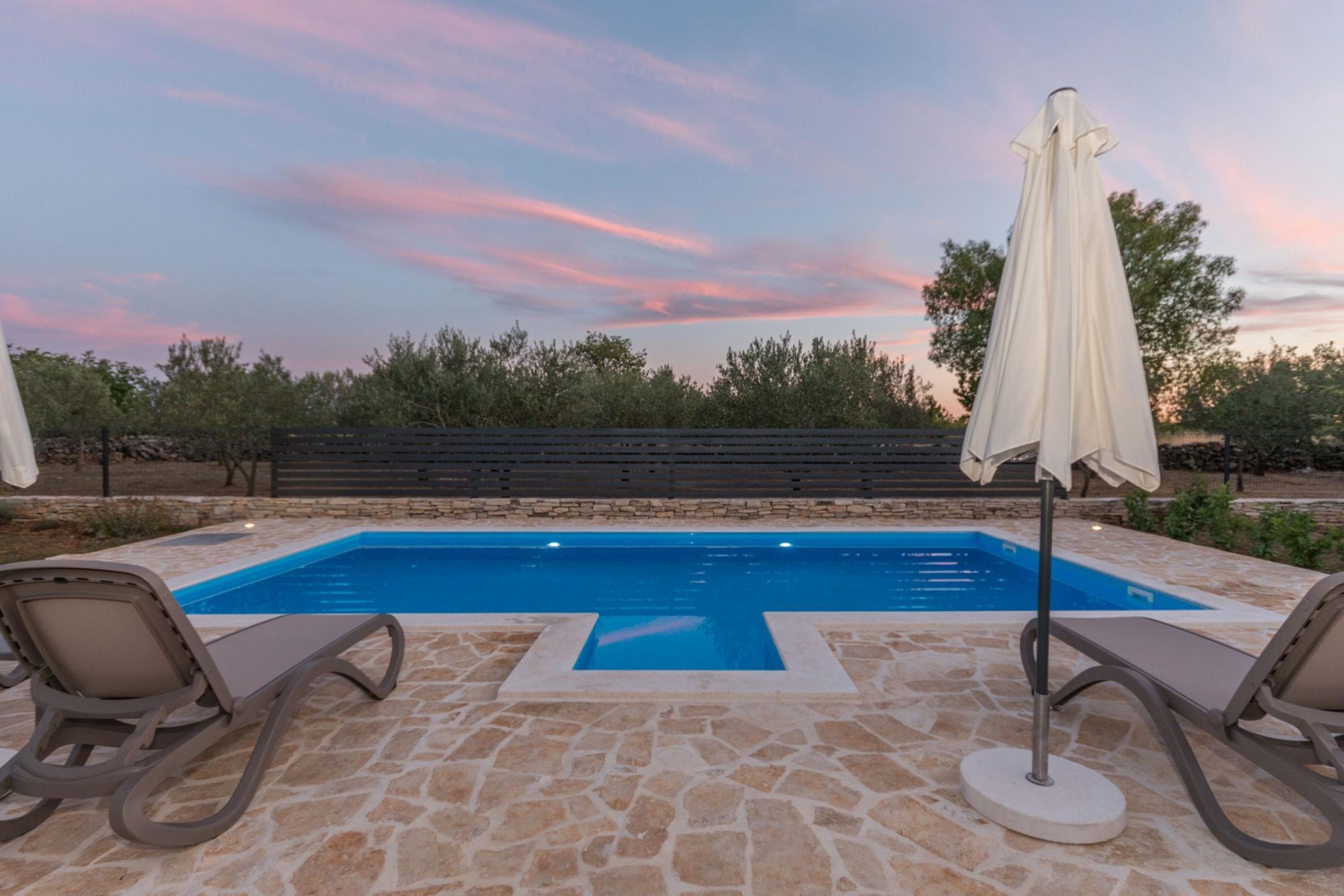 Una piscina con baldosas de piedra, dos sillas de descanso y una sombrilla.