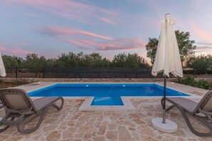 A swimming pool with stone tiles, two lounge chairs, and an umbrella. - Villa Vitis Zadarvillas (Promina)