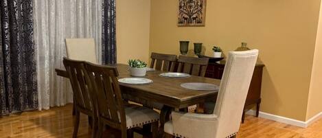 Un comedor con una mesa y sillas de madera, una planta en maceta y un adorno en la pared.