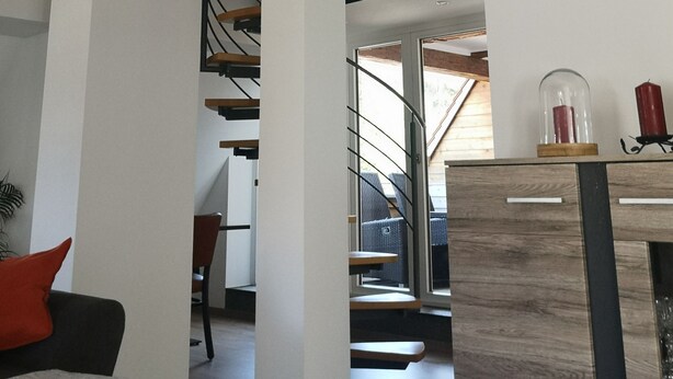 A spacious loft with exposed wooden beams, a staircase, and a view of the outdoors.