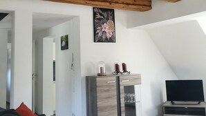 A modern living room with exposed wooden beams, a flat-screen TV, a wooden cabinet, and a large window.