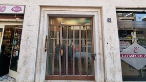 Un edificio con un amplio acceso por puerta de vidrio, fachada de ladrillo y una tienda con un letrero que dice 'LAVASECCO &'.
