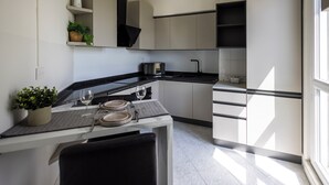 Una cocina moderna con armarios blancos, encimera negra y una zona de comedor con una mesa dispuesta para dos personas.