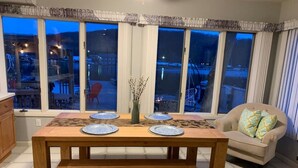 Een eethoek met een houten tafel gedekt voor twee personen, een bank en uitzicht op een besneeerd landschap door grote ramen.
