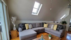 Een moderne woonkamer met een grijze modulaire bank, een houten salontafel en een dakraam erboven.