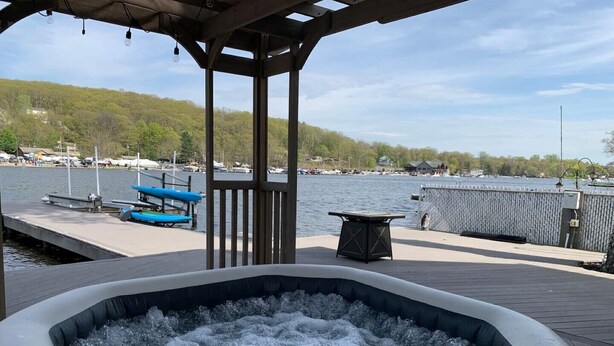 Een hottub op een houten terras met uitzicht op een jachthaven en heuvels op de achtergrond.