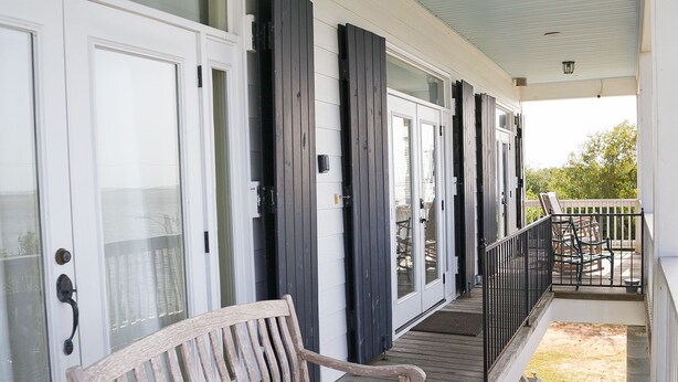A covered porch with a wooden bench, white doors, and a black railing.