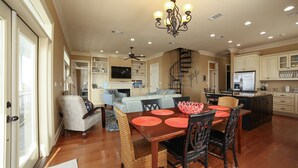 A spacious kitchen with a central island, a dining area with a wooden table and chairs, and a living area with a sofa and a TV.