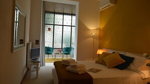 Hotelkamer met een bed, een bureau met een computer, een stoel en een raam met decoratieve ijzeren tralies.