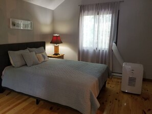 Een slaapkamer met een bed, een nachtkastje, een lamp, een verwarming en een raam met gordijnen.