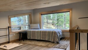 A bedroom with a bed, a desk, and large windows offering a forest view.