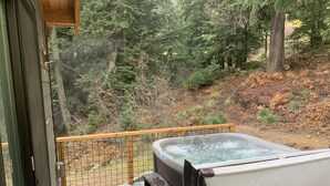 A hot tub on a wooden deck with a view of a forested hillside.