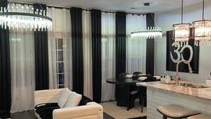 A modern living room with a sofa, a dining area with a table and chairs, and a kitchen island with stools.