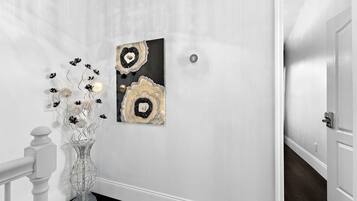 A hallway with a white wall, a black and gold abstract painting, and a clear glass vase with flowers.