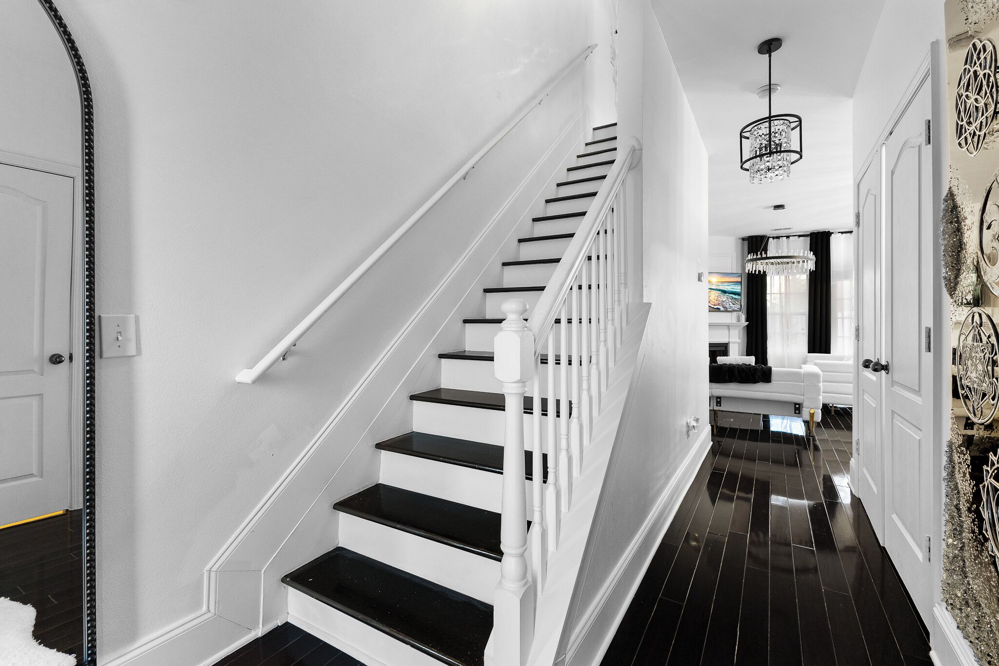 A staircase with white railings and black steps, leading to a room with a white door and a chandelier.