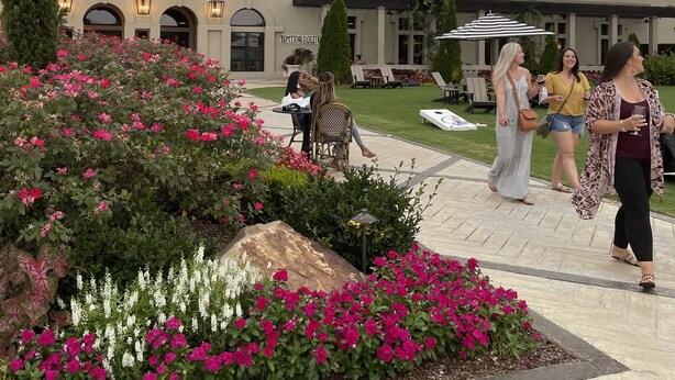 A building with a prominent tower and arched windows, surrounded by a well-maintained garden with pink flowers.