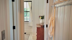 A hallway with white paneled walls, a wooden dresser, and a hanging broom.
