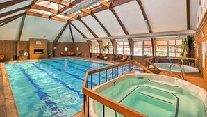 Ein Hallenbad mit hoher Decke und Dachfenstern, einem Whirlpool und Liegestühlen am Pool.