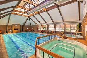 Piscina interior con techos altos y tragaluces, bañera de hidromasaje y sillones de descanso junto a la piscina.