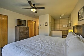 Habitación de hotel con cama, cómoda, ventilador de techo, televisor y baño visible a través de una puerta abierta.