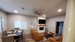 A modern living room with a fireplace, a dining area with a table and chairs, and a ceiling fan. - Beach house 3BR/3.5BA 5 minute walk to bay with extra parking for a boat/RV (Navarre)