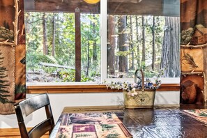 Un coin repas rustique avec une table en bois, des chaises et une fenêtre donnant sur la forêt.