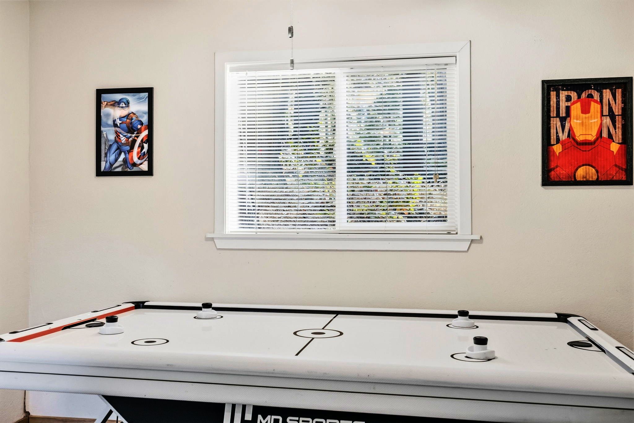 A pool table with a window above it, flanked by two framed posters, one of which is a character from a popular film franchise.