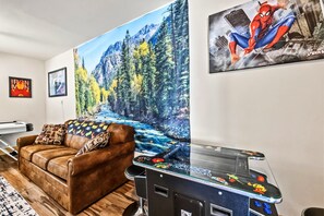 Una habitación con un sofá de cuero marrón, un cuadro grande de un río en un bosque y un póster de Spiderman en la pared.