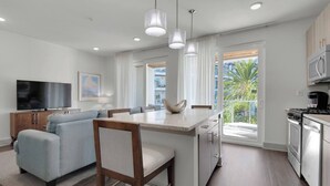 A modern kitchen with a central island, a dining area with a sofa, and a TV in the living room.