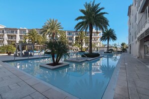 Ein Swimmingpool mit Palmen, Liegestühlen und einem Gebäude mit Balkonen im Hintergrund.