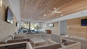 A modern lounge area with white furniture, wooden ceiling panels, and a large TV screen.