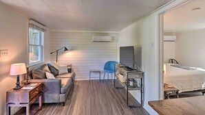 Une pièce de taille modeste comprenant un canapé, une petite table, une chaise bleue, un lit et un appareil de climatisation.