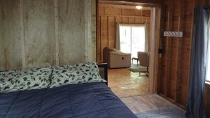 A wooden cabin interior with a bed, a sofa, and a dining area.
