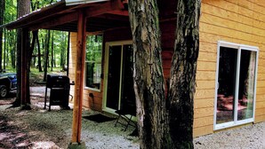 A wooden cabin with a covered porch, large windows, and a grill outside.