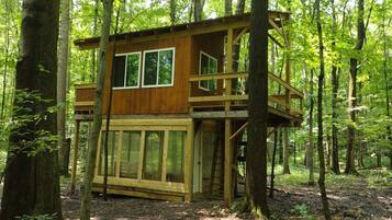 Une cabane en bois perchée dans un arbre, dotée d’un balcon et d’une échelle, et entourée d’une forêt.