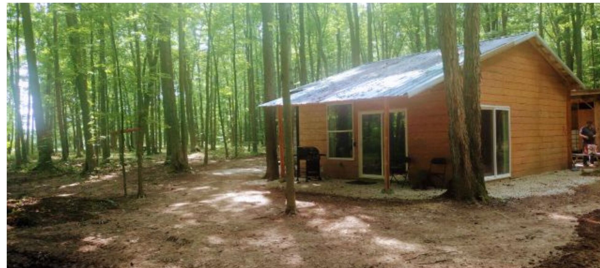 Una cabaña en un bosque con suelo de tierra y árboles altos.