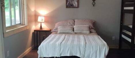 A bedroom with a bed, a nightstand, a lamp, a framed picture, and a window.